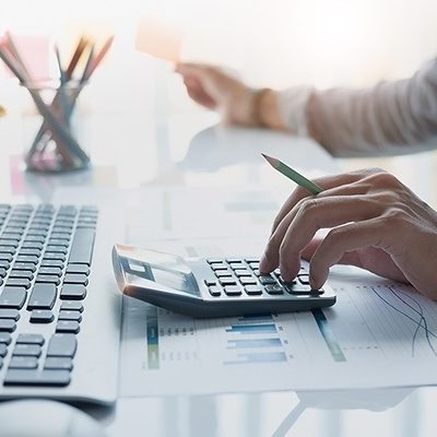 Close up of businessman or accountant hand holding pencil working on calculator to calculate financial data report, accountancy document and laptop computer at office, business concept